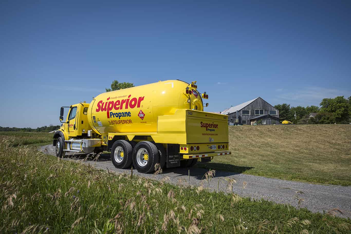 A Superior Propane truck driving up a road towards a farm in the background.