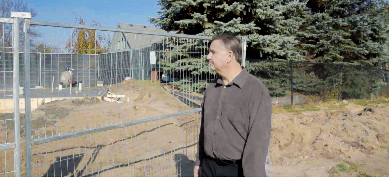 Man gazes at his dug up lawn from behind a fence